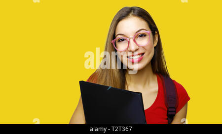 Junge schöne Mädchen hält schwarzes Papier Ordner in der Hand und Lächeln, auf gelben Hintergrund. Gerne student Cames zurück zu scool und sie ist froh zu sehen Stockfoto