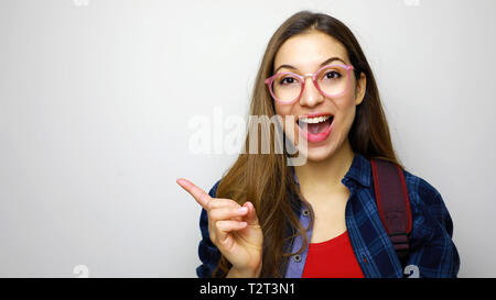 Studio shot der positiven Schüler Mädchen auf weißem Hintergrund Brillen und Rucksack, Zeigefinger auf der Suche aufgeregt Stockfoto