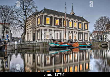 Schiedam, Niederlande, 11. Februar 2019: Der ehemalige Corn Exchange Gebäude, jetzt öffentliche Bibliothek und einen historischen Lastkahn spiegeln sich im Wasser des Stockfoto