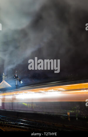 Atmosphärisch, Moody Nacht und beweglichen UK Dampflok durch Vintage Railway Station in der Nacht unterwegs. Lange Belichtung: Bewegung, Bewegungsunschärfe. Stockfoto