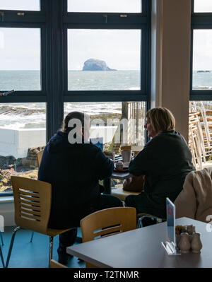 North Berwick, East Lothian, Schottland, Vereinigtes Königreich, 4. April 2019. Scottish Seabird Centre öffnet wieder nach 3-monatiger Renovierung und Sanierung. Das Cafe Bereich hat mehr neben Windows. Ein paar sitzen im neu renovierten Cafe mit Bass Rock am Horizont Stockfoto