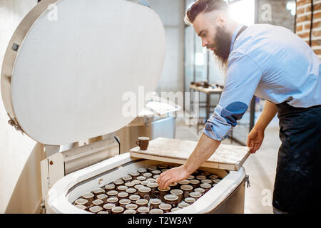 Mann, gebackene Keramik Tassen aus dem Backofen an der Töpferei Fertigung Stockfoto