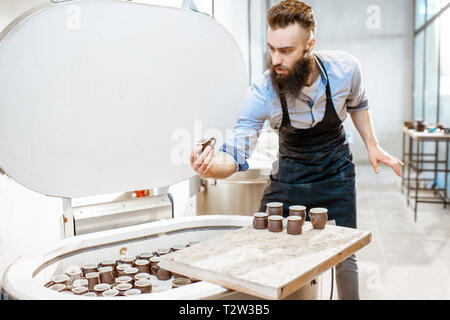 Mann, gebackene Keramik Tassen aus dem Backofen an der Töpferei Fertigung Stockfoto