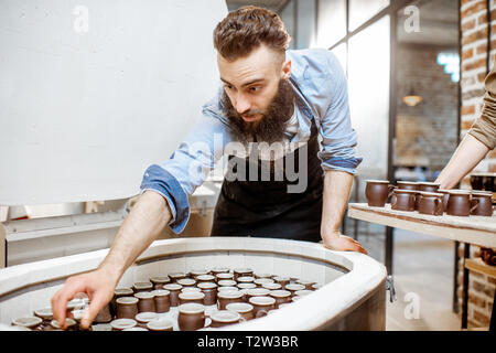 Mann, gebackene Keramik Tassen aus dem Backofen an der Töpferei Fertigung Stockfoto