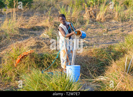 Malawische Frau zieht Wasser aus flachen gut mit einem Seil und Paint tin Stockfoto