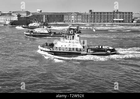 Schwarz-weiß-Foto von 3 SERCO LTD, Schlepper, die der Royal Navy Aircraft Carrier, HMS QUEEN ELIZABETH, bei der Abfahrt von Portsmouth Harbour, Großbritannien, helfen Stockfoto