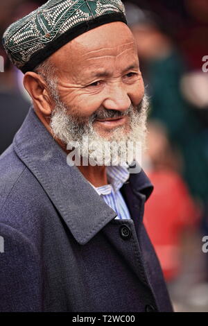 Bärtiger Uyghur-Mann mit Doppelkappe auf dem Basar der Stadt. Hotan-Xinjiang-China-0076 Stockfoto