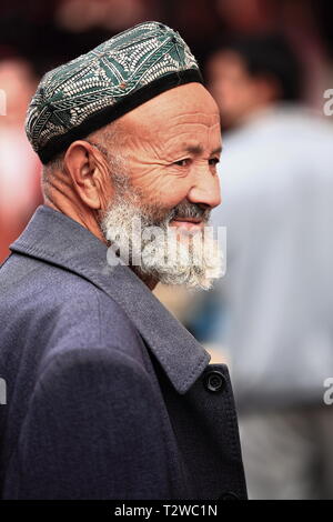 Bärtiger Uyghur-Mann mit Doppelkappe auf dem Basar der Stadt. Hotan-Xinjiang-China-0077 Stockfoto