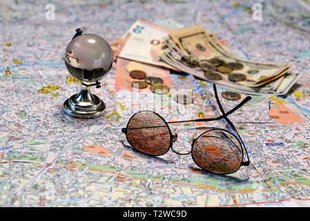 Sonnenbrille, ein glas kugel und Geld auf eine touristische Karte Hintergrund. Tourismus Konzept. Stockfoto