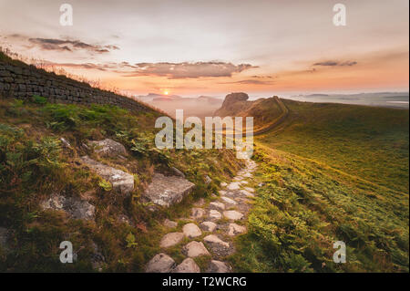 Northumberland National Park. Dawn auf dem Weg in der Nähe von Cuddy Craig auf Hadrian's Wall auf der Suche nach Osten in Richtung Housesteads Craig und die aufgehende Sonne. Stockfoto