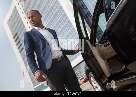 Junge afrikanische amerikanische Mann stand in der Nähe der Car holding Tür beiseite, Schielen, Ansicht von unten Stockfoto