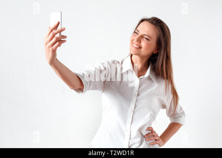 Reife Frau, die isoliert auf die weiße Wand unter selfie Fotos auf dem Smartphone posiert für die Kamera lächelt Fröhlich Stockfoto