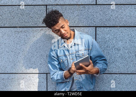 Junge afrikanische amerikanische Mann stehend auf Betonwand im Internet surfen auf digitalen Tablet isoliert konzentriert Stockfoto