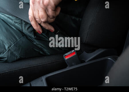 Ältere ältere Frau befestigt ein Sicherheitsgurt in ein Auto mit grünen und gelben Jacke - Kein leder Limousine Stockfoto