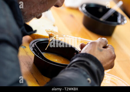 Ältere Mensch isst warme Suppe mit Brot in einer Küche mit kostenlosem Essen für Arme und Obdachlose. Stockfoto