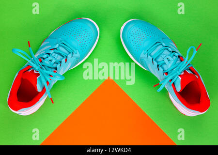 Rot, hellblau, weiß, Paar neue Tennisschuhe im Studio Schuß über grün und orange hinterlegt. Direkt von oben. Stockfoto