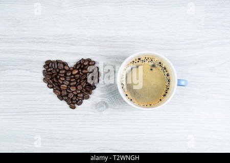 Liebe Kaffee, eine Herzform aus Kaffeebohnen neben einer Tasse Kaffee auf einen hölzernen Tisch. Kann als Hintergrund verwendet werden Stockfoto