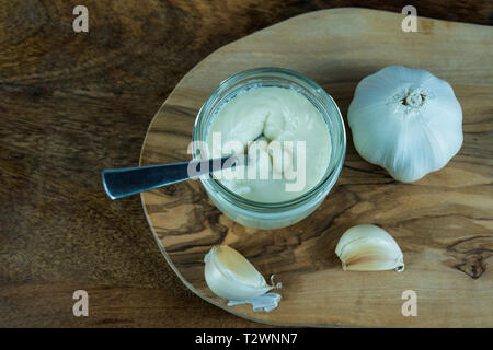 Blick von oben auf die Olivenöl Knoblauch auf einer Holzplatte. auf der Holzplatte ist ein Glas mit hausgemachter Aioli Stockfoto