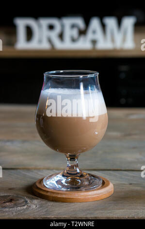 Glas mit Cappuccino auf einer hölzernen Tisch. Auf dem Hintergrund das Wort Traum Stockfoto