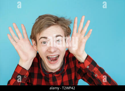 Junge männliche Teenager im roten Hemd auf blauem Hintergrund belauscht Aprilscherze Stockfoto