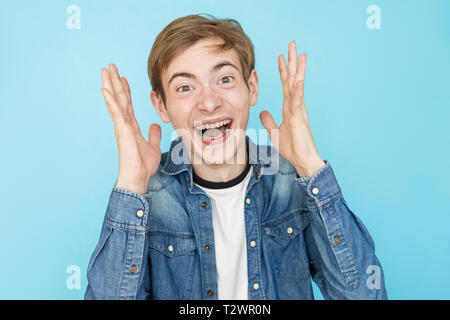 Junge emotionale Lustige männliche Teenager in jeanshemd auf blauem Hintergrund Stockfoto