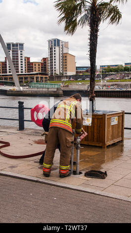 Ein Feuerwehrmann Bekämpfung eine brennende Palme am Kai, Newcastle upon Tyne, England, UK. Drehen auf Wasser Hydranten. Stockfoto