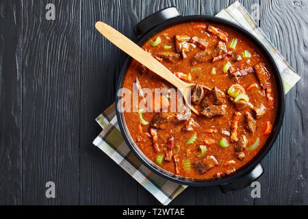 Klassisches irisches Rindfleisch und Bier Eintopf mit Karotten, Speck, Sellerie, Karotten und Gewürze in einem holländischen Ofen, Ansicht von oben, flatlay, kopieren Raum Stockfoto