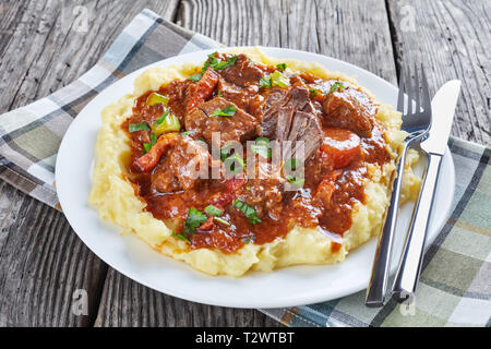 Irisches Rindfleisch Eintopf mit Kartoffelpüree auf einem Teller mit Besteck und Serviette auf einem Holztisch, Ansicht von oben, close-up Stockfoto