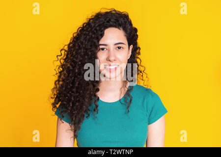 Hübsches Mädchen mit Curly Frisur auf gelben Hintergrund. Schöne Portrait der Frau in Grün t-shirt lächelnd und mit Blick auf die Kamera. Latein oder Hispanic r Stockfoto