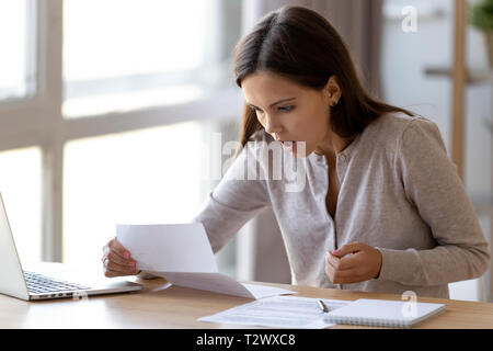 Überrascht junge Frau sitzt am Schreibtisch lesen schreiben Stockfoto