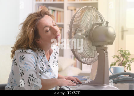 Frau leidet unter der Hitze, während der Arbeit im Büro und versucht durch den Lüfter zu kühlen Stockfoto