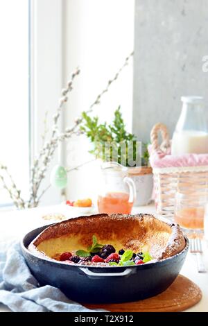 Frische hausgemachte Niederländische baby Pfannkuchen mit Puderzucker, frische Beeren und Minze zum Frühstück mit einem Glas Milch und Apfelsaft auf einen hellen Hintergrund Stockfoto