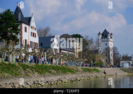 Eltville, Deutschland - 31. März 2019: River Promenade in Eltville mit Menschen an einem sonnigen Tag mit Blick auf das Schloss. Stockfoto