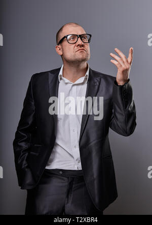 Konzentriert kahlen business Mann suchen der Schwere in Brillen und haben eine Idee in der Klage auf grauem Hintergrund. Closeup studio Portrait Stockfoto