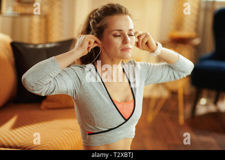 Relaxed Fit Frau in Fitness Kleidung in der modernen Wohnzimmer Kopfhörer tragen. Stockfoto