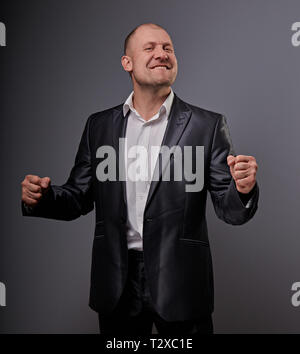 Verlassen kahlen business Mann im schwarzen Anzug, der die Hände erfolg Sieger Zeichen auf grauem Hintergrund. Closeup Portrait Stockfoto