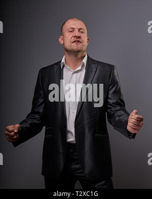 Verlassen comic Kahlen business Mann im schwarzen Anzug, der die Hände erfolg Zeichen auf grauem Hintergrund. Closeup Portrait Stockfoto