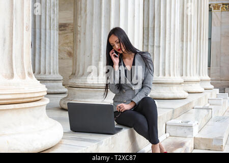 Elegante Frau im Gespräch mit Mobile beim Arbeiten mit Ihrem Laptop Stockfoto