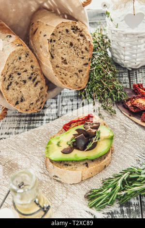 Hausgemachtes Brot mit Oliven und getrockneten Tomaten, Avocado und Olivenöl. Stockfoto