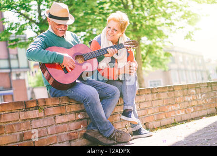 Gerne älteres Paar Spielen einer Gitarre, während draußen auf einer Wand an einem sonnigen Tag - Konzept der aktiven älteren Menschen Spaß mit Gitarre Stockfoto