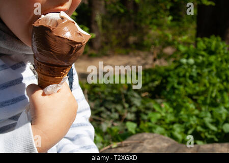 Niedliche Kind essen Kegel Schokolade Eis im Sommer in einem Park. Kleines Kind, kleine Hand, kein Gesicht, Nahaufnahme Stockfoto