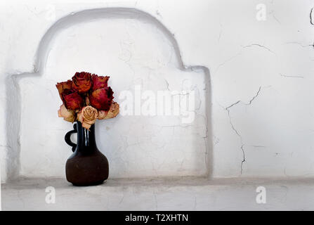 Trockene Rosen in einer Vase aus Keramik in der Wand Nische Stockfoto