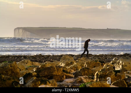 Person zu Fuß auf einem Strand in Sussex bei Sonnenuntergang. Stockfoto