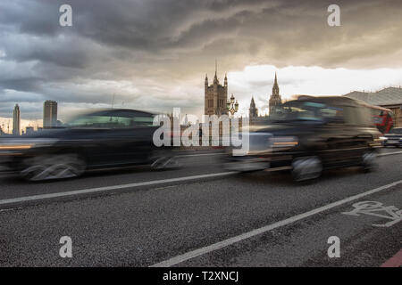 Westminster, London, England, 3. April 2019. Die berühmten schwarzen Taxis und anderen Verkehr Westminster Bridge mit den Häusern des Parlaments an der Bac Stockfoto