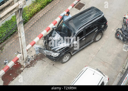 Bangkok, Thailand - 12. Dezember 2018: ein Auto Besitzer macht einen Anruf nach Absturz mit seinem Wagen gegen einen Strommast in einem leeren Backstreet. Stockfoto