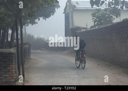Ein kleines Kind ist mit dem Fahrrad durch eine Landstraße am frühen Winter morgen Stockfoto