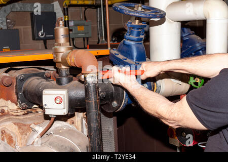 Kessel Ingenieur mit einem Schraubenschlüssel ein Rohr aus einem Sicherheitsventil auf einer sehr alten Gaskessel Gas zu entfernen. Stockfoto