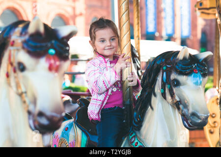 Wenig liebenswert lächelnde Mädchen ein Pferd Reiten am Kreisverkehr Karussell an Kirmes Stockfoto