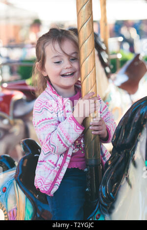 Wenig liebenswert lächelnde Mädchen ein Pferd Reiten am Kreisverkehr Karussell an Kirmes Stockfoto