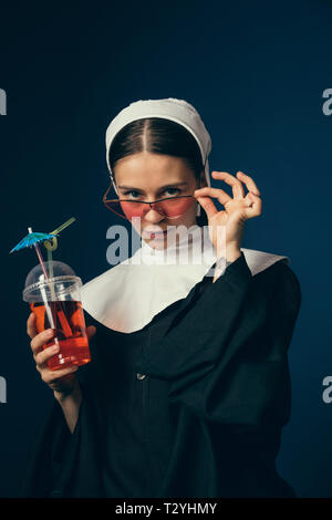 Mittelalterliche Bar und im Sommer. Junge Frau als Nonne in Vintage Kleidung und weiß mutch auf dem Stuhl auf dunkelblauem Hintergrund. Trinken lemonad o Stockfoto